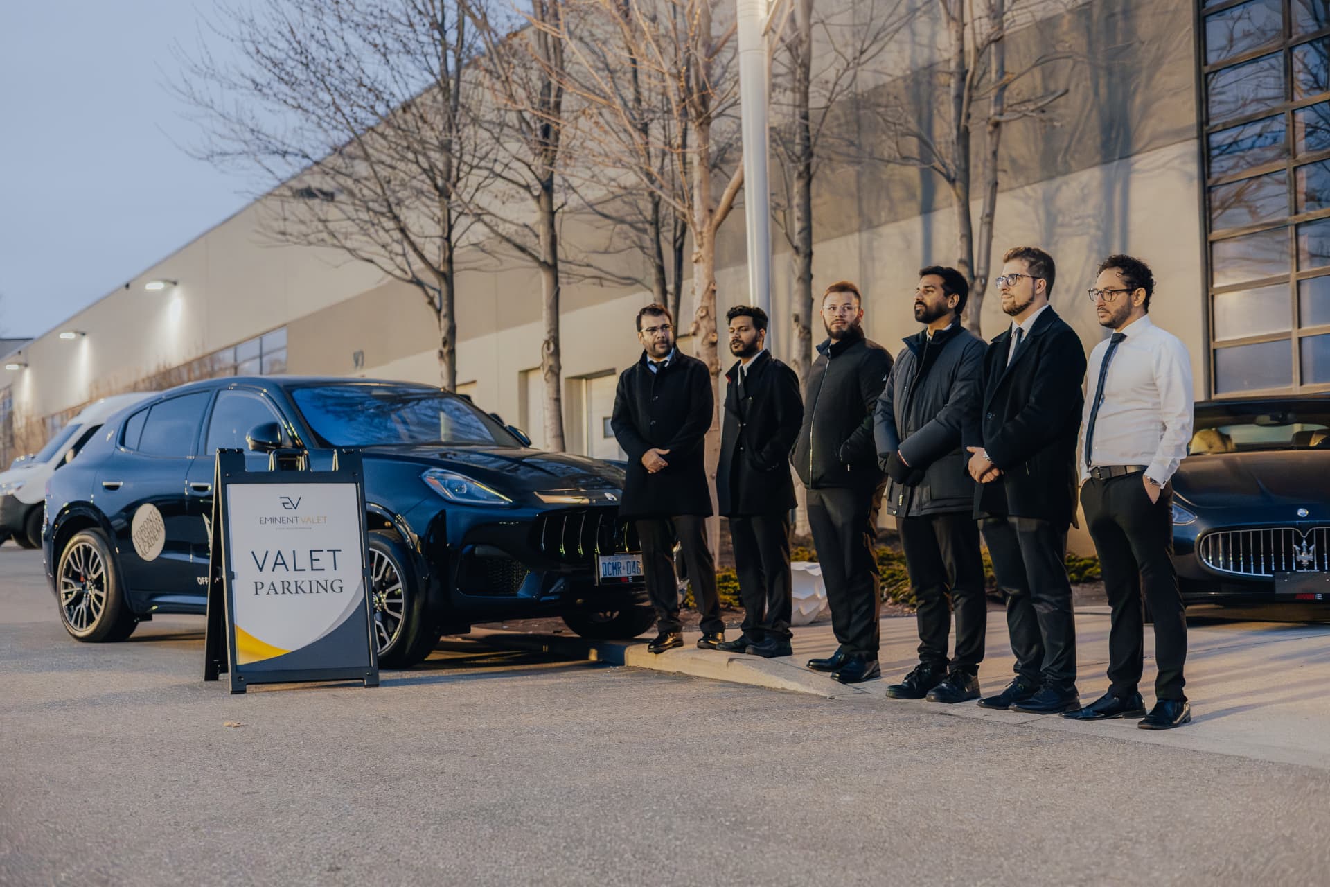 Eminent Valet event team standing by a valet parking sign beside luxury vehicles at dusk